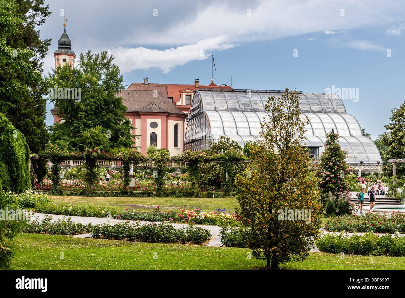Sur l'île aux fleurs de Mainau près de Constance, dans le Bade-Württemberg, en Allemagne, les visiteurs apprécient les magnifiques jardins avec l'église du château historique de Sainte-Marie et l'imposante Palm House en arrière-plan Banque D'Images Sur l'île aux fleurs de Mainau près de Constance, dans le Bade-Württemberg, en Allemagne, les visiteurs apprécient les magnifiques jardins avec l'église du château historique de Sainte-Marie et l'imposante Palm House en arrière-plan Banque D'Images