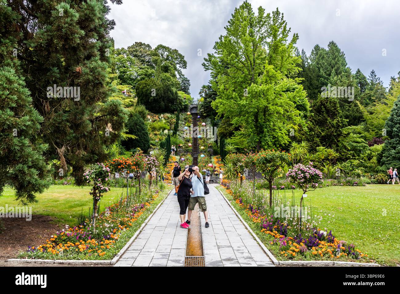 Les visiteurs explorent le magnifique jardin en terrasses sur l'île de Mainau sur le lac de Constance près de Constance, en Allemagne. Ils apprécient la splendeur florale variée, les grands arbres, les caractéristiques aquatiques de l'escalier d'eau de fleurs italiennes et les boules colorées décoratives qui ornent le terrain Banque D'Images Les visiteurs explorent le magnifique jardin en terrasses sur l'île de Mainau sur le lac de Constance près de Constance, en Allemagne. Ils apprécient la splendeur florale variée, les grands arbres, les caractéristiques aquatiques de l'escalier d'eau de fleurs italiennes et les boules colorées décoratives qui ornent le terrain Banque D'Images