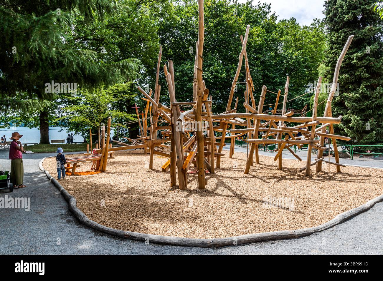 Enfants et adultes profitent d'une journée ensoleillée sur une aire de jeux en bois naturel sur l'île de Mainau, en Allemagne. L'aire de jeux est située directement sur les rives du lac de Constance et offre un cadre pittoresque pour jouer et se détendre en Europe Banque D'Images Enfants et adultes profitent d'une journée ensoleillée sur une aire de jeux en bois naturel sur l'île de Mainau, en Allemagne. L'aire de jeux est située directement sur les rives du lac de Constance et offre un cadre pittoresque pour jouer et se détendre en Europe Banque D'Images