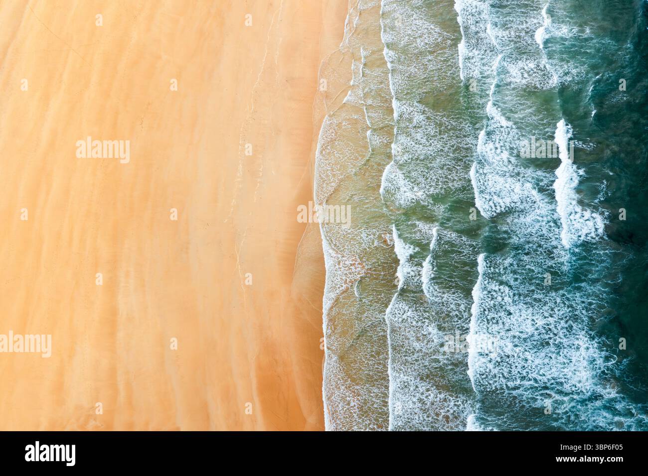 Vue aérienne de haut en bas d'une plage de sable ensoleillée avec de douces vagues blanches mousseuses Banque D'Images