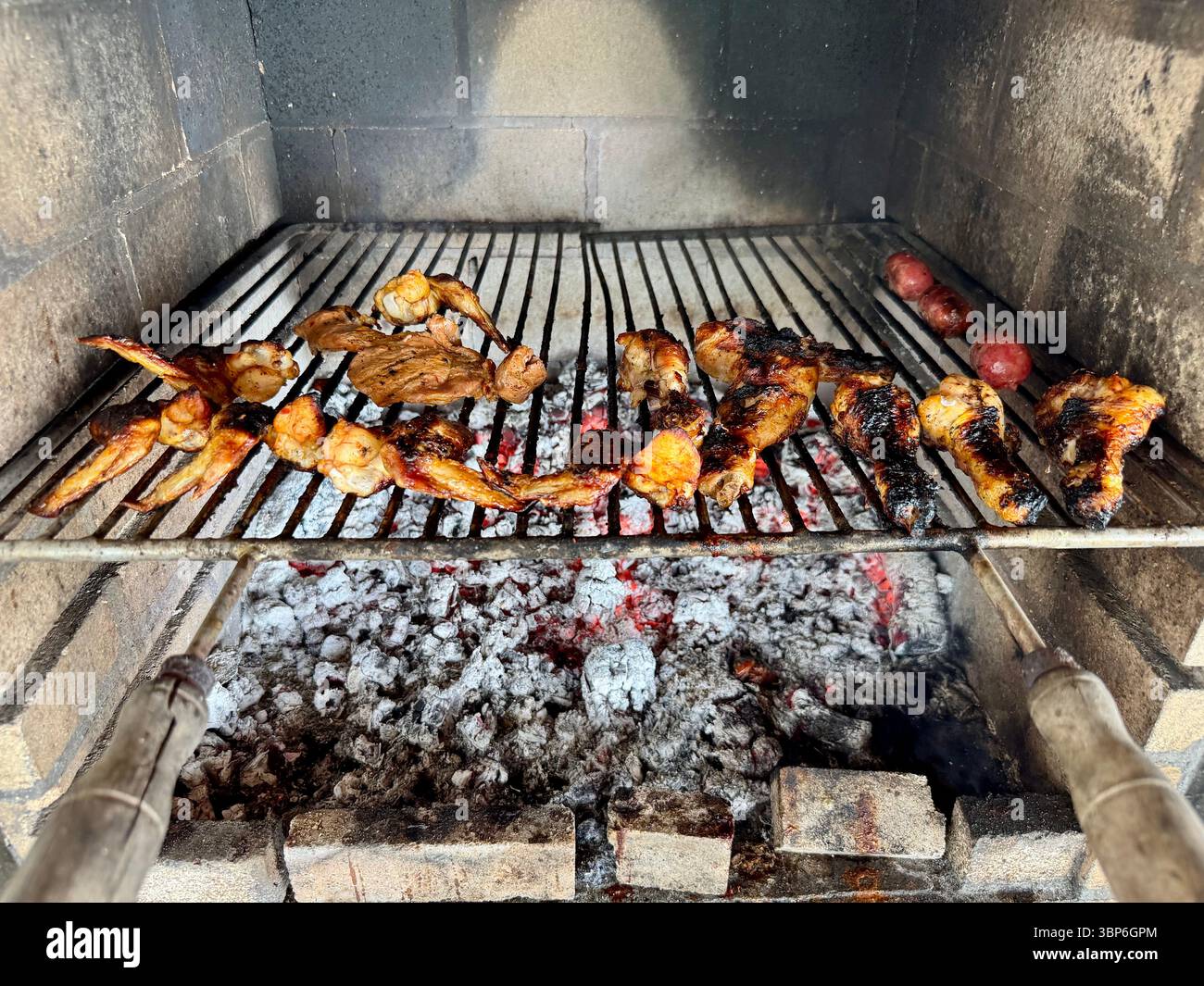 Assortiment de viandes grésillant sur un gril à charbon de bois au-dessus de braises incandescentes. Banque D'Images
