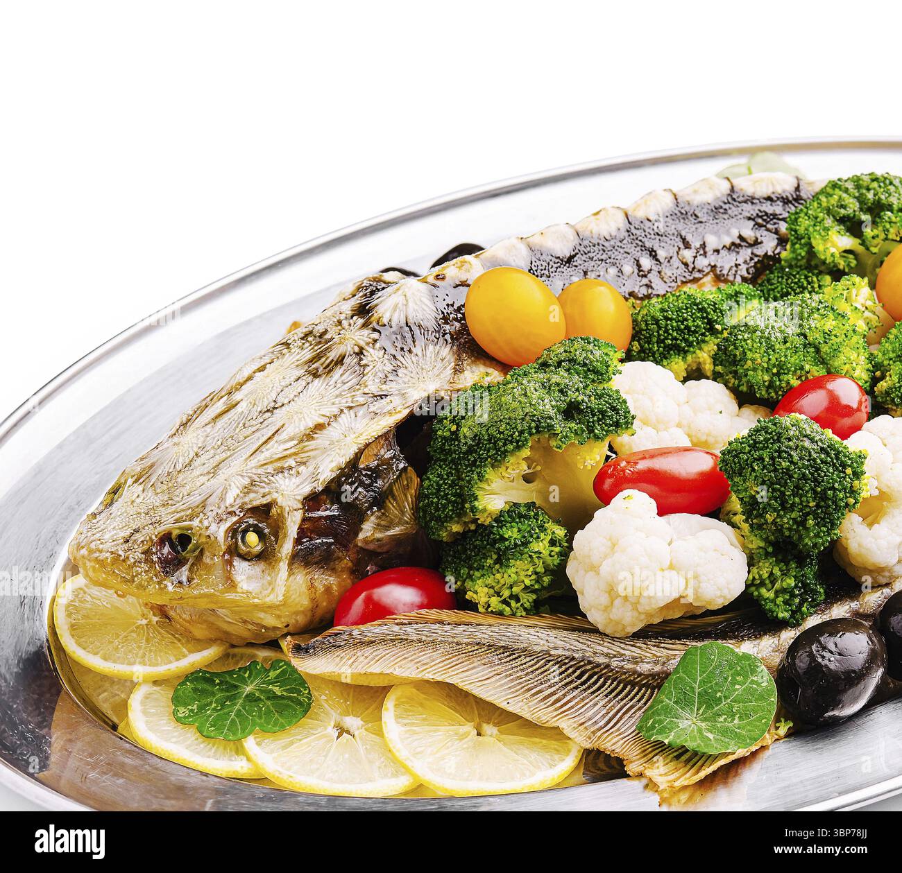 Nourriture, Un poisson grillé magnifiquement présenté repose sur un plateau d'argent, accompagné de légumes vibrants comme le brocoli, le chou-fleur et la tomate cerise Banque D'Images