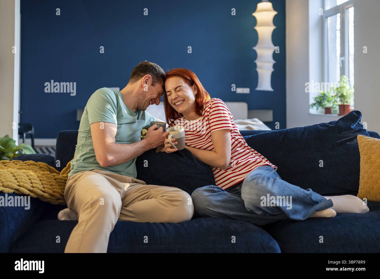 Heureux jeune couple insouciant dans l'amour plaisanter en riant tout en se relaxant sur le canapé avec du café, se lier, profiter du temps du matin ensemble à la maison. Co. Émotionnelle Banque D'Images