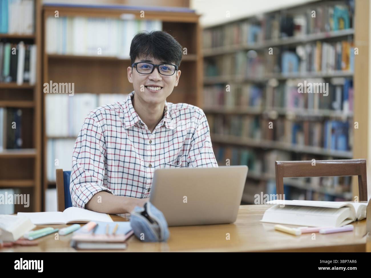 Jeune étudiant asiatique faisant de la recherche à l'intérieur d'une bibliothèque seul. Jeune homme assis et travaillant sur un projet. Homme concentré lisant et écrivant Banque D'Images