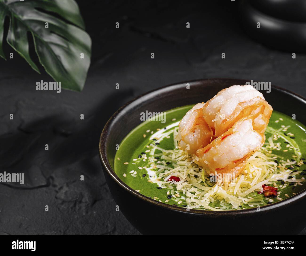 Nourriture, présentation gourmande de soupe de crevettes aux épinards ornée de garnitures dans un bol sombre sur une surface texturée Banque D'Images
