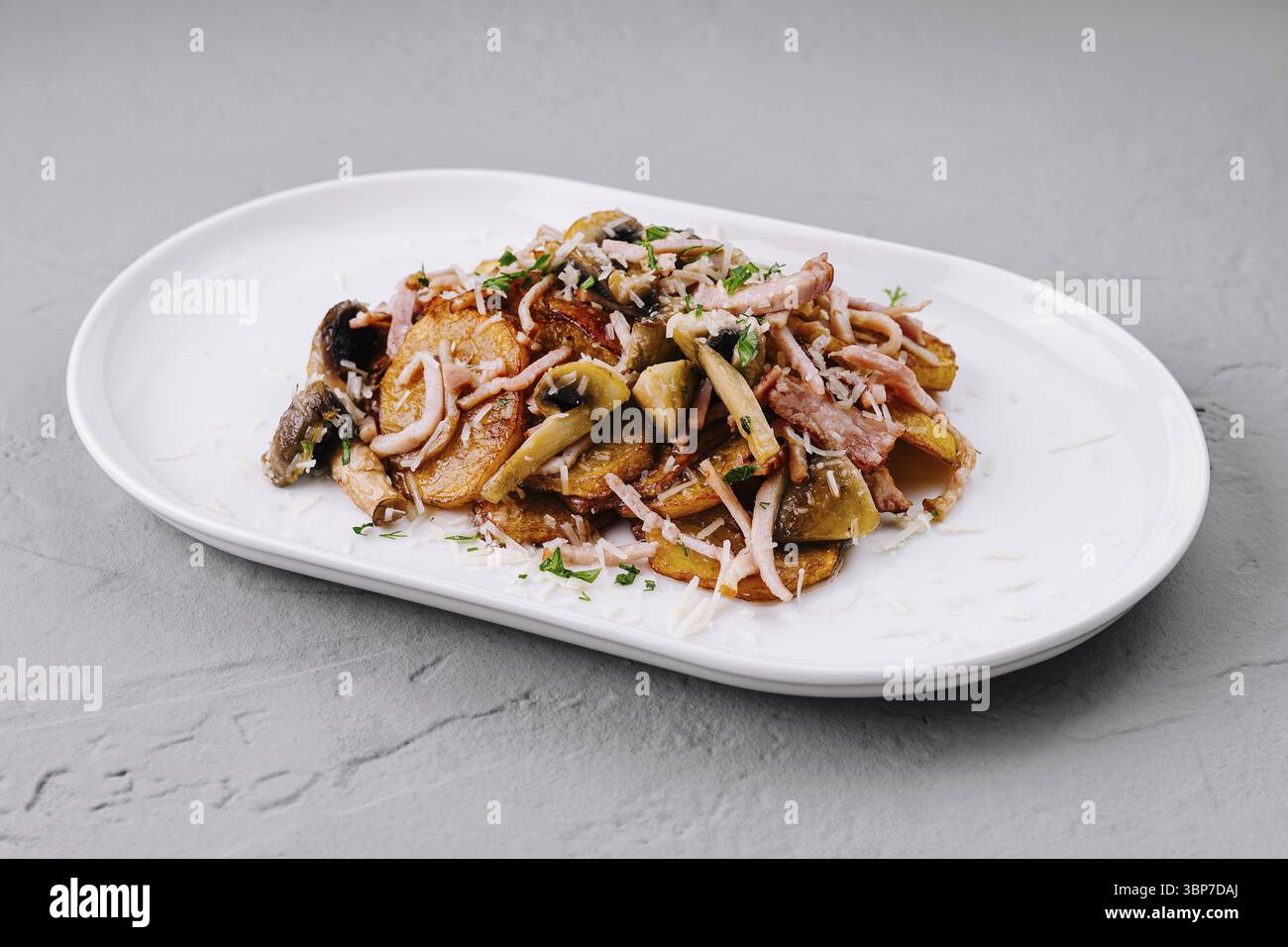 Nourriture, pommes de terre rôties avec bacon et champignons assaisonnés de parmesan râpé et de persil sur une assiette blanche Banque D'Images