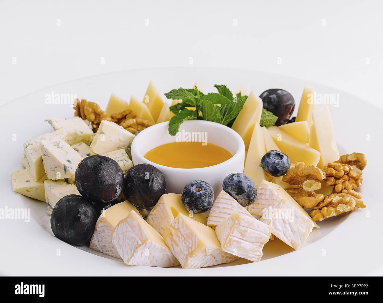 Nourriture, assiette de fromage élégante avec une variété de fromages, noix, myrtilles, et un bol de miel, isolé sur blanc Banque D'Images