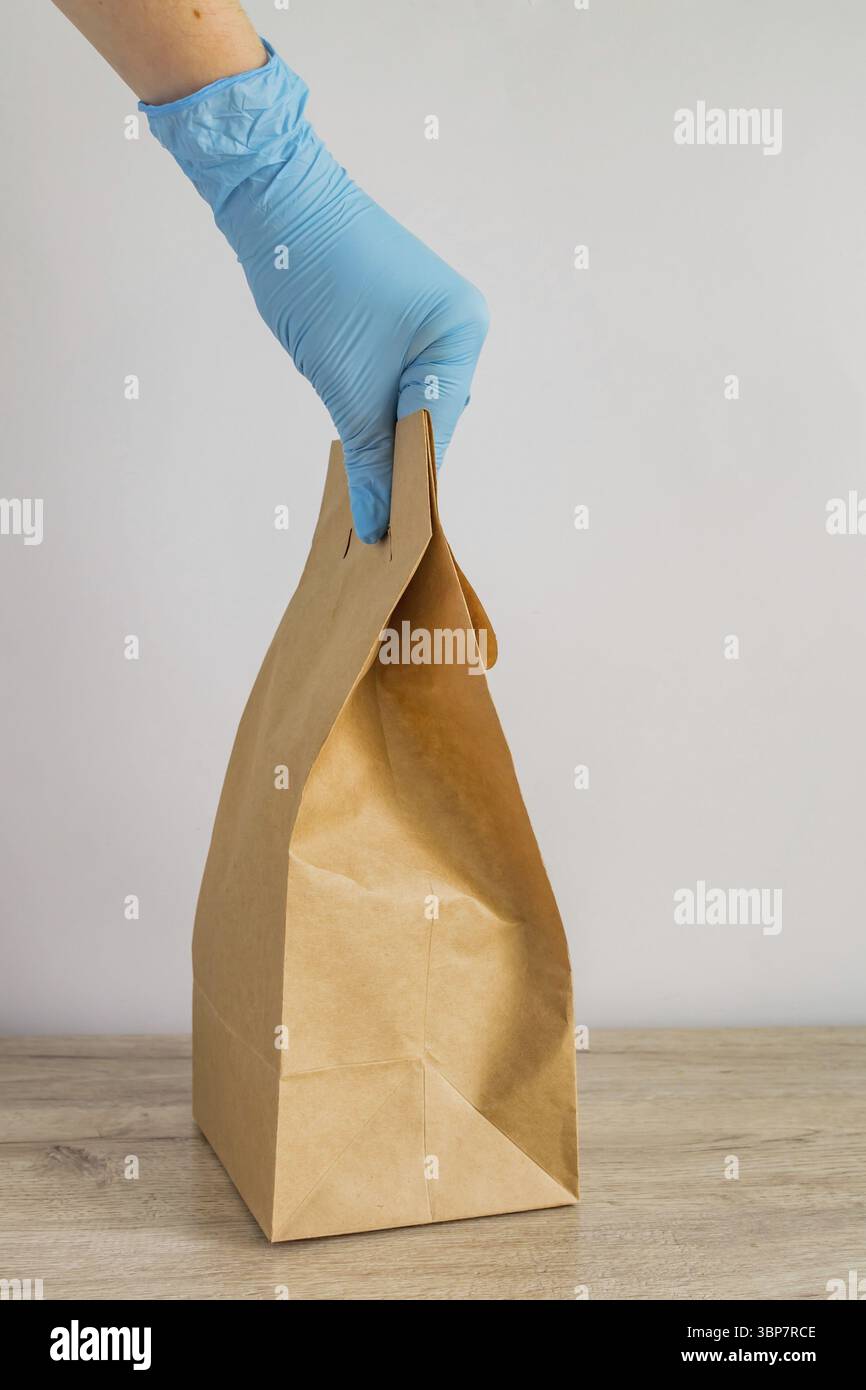 Main de femme dans des gants en latex bleu tenant le sac en papier jetable artisanal pour la livraison. Accouchement sans danger lors de l'isolement du coronavirus Banque D'Images