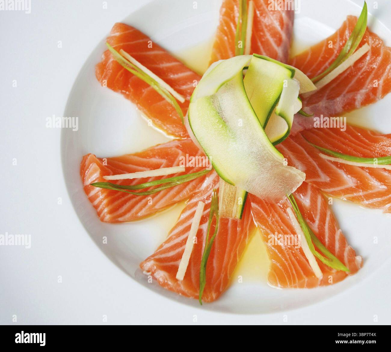 Nourriture, délicieuses tranches de sashimi de saumon cru disposées sur une assiette blanche, ornées d'un délicat ruban de concombre Banque D'Images