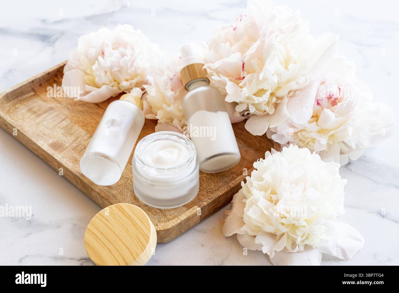 Crème, sérum, essence, huile dans un emballage en verre givré avec des fleurs de pivoine roses. Plateau en bois de produit cosmétique de soin de la peau. Foyer sélectionné Banque D'Images
