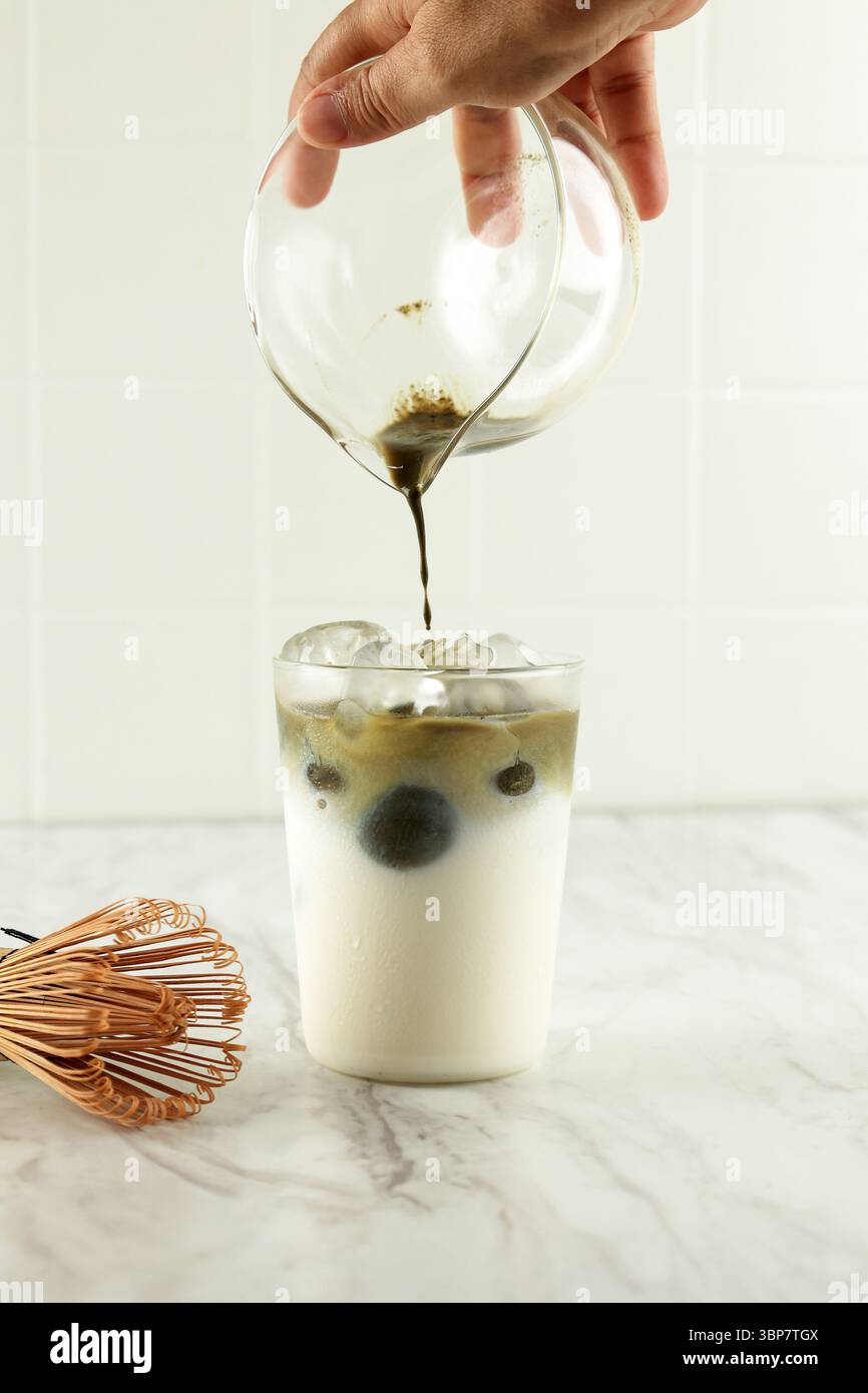 Le thé Matcha est versé dans du lait glacé. Boisson végétalienne saine Matcha Latte Banque D'Images