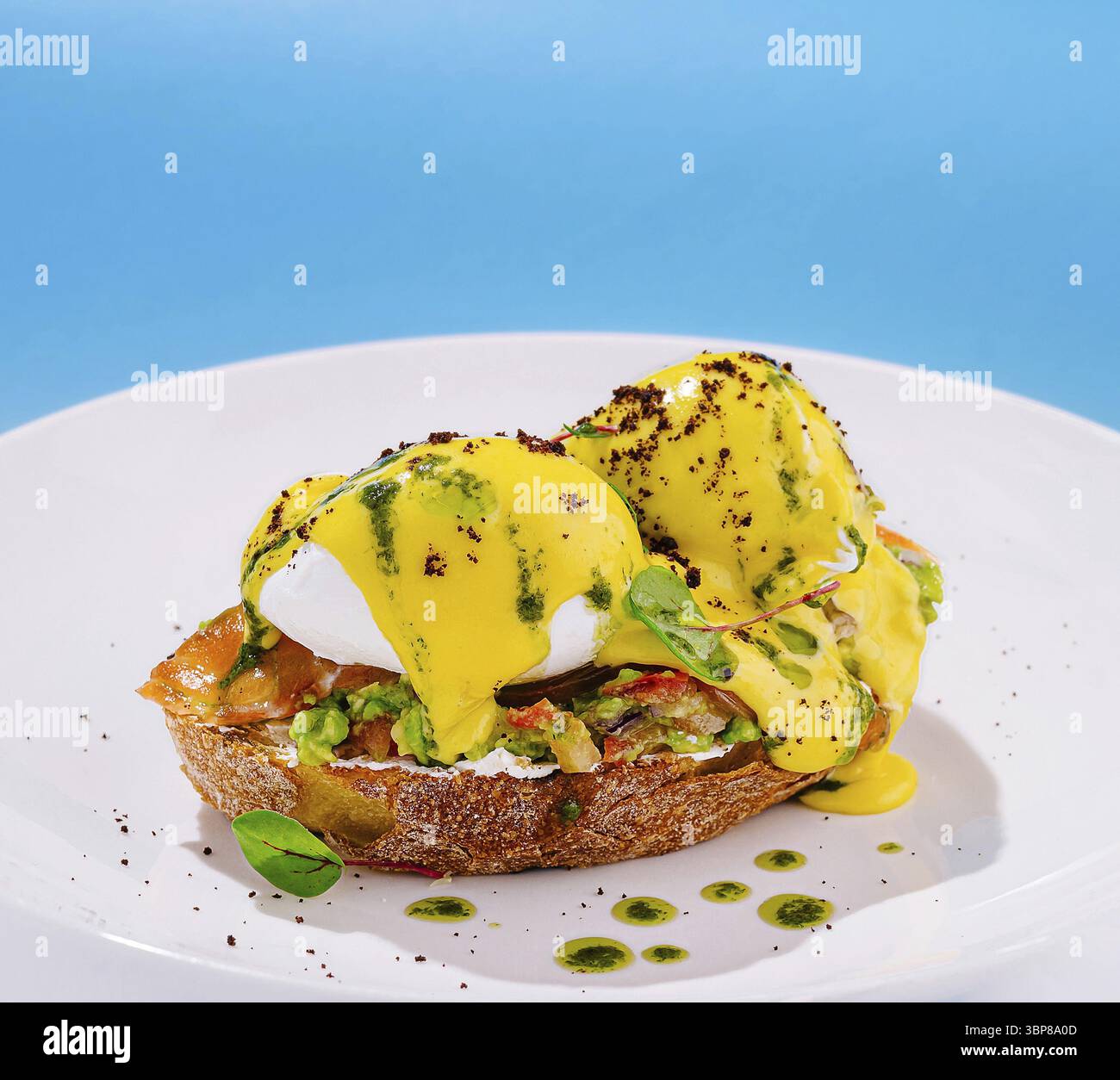 Nourriture, deux œufs parfaitement pochés assis sur le pain grillé avec avocat et saumon, arrosé d'une sauce jaune crémeuse et entouré d'herbes fraîches Banque D'Images
