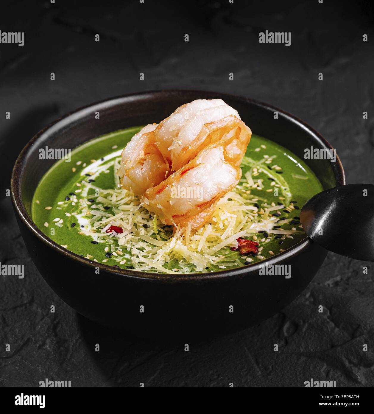 Nourriture, présentation gourmande de soupe de crevettes aux épinards ornée de garnitures dans un bol sombre sur une surface texturée Banque D'Images