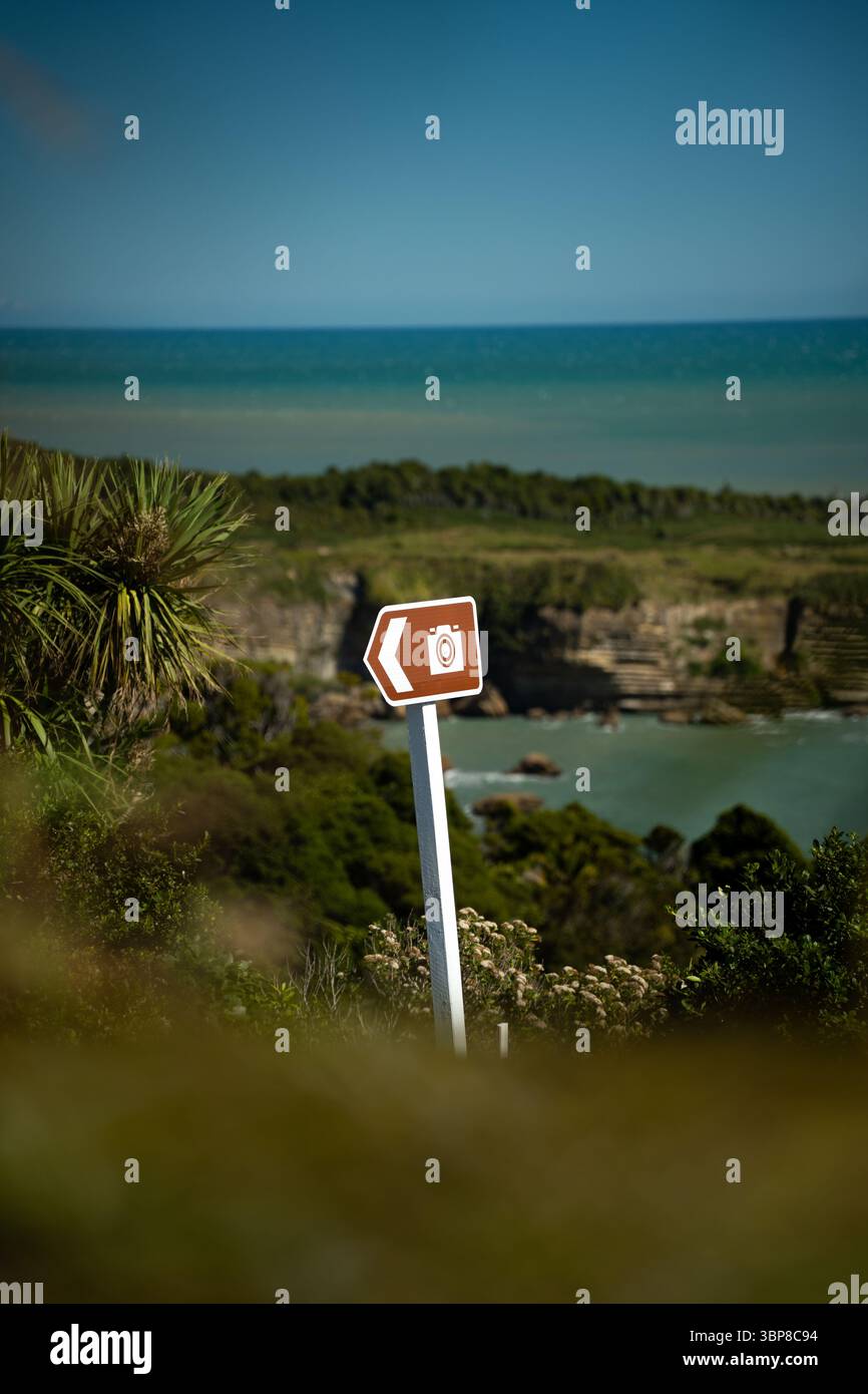 Un panneau marron de point de vue pittoresque avec une icône de caméra se dresse sur un fond de verdure côtière luxuriante et de mer turquoise, invitant les voyageurs à s'arrêter et Banque D'Images