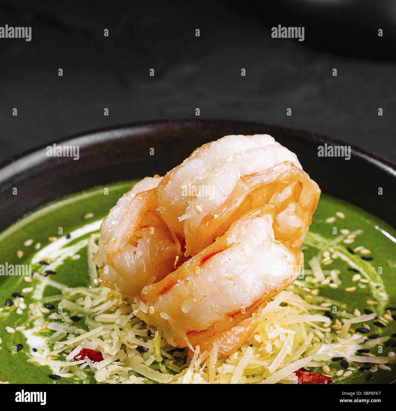 Nourriture, présentation gourmande de soupe de crevettes aux épinards ornée de garnitures dans un bol sombre sur une surface texturée Banque D'Images