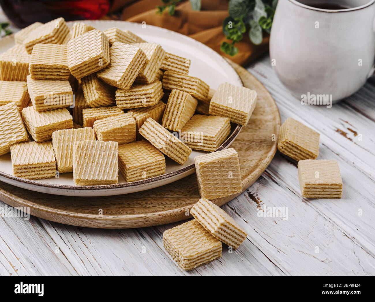 Nourriture, Une assiette empilée de gaufrettes croustillantes dorées repose sur une surface en bois. Une tasse de boisson chaude se trouve à proximité, invitant à profiter des collations sucrées i. Banque D'Images