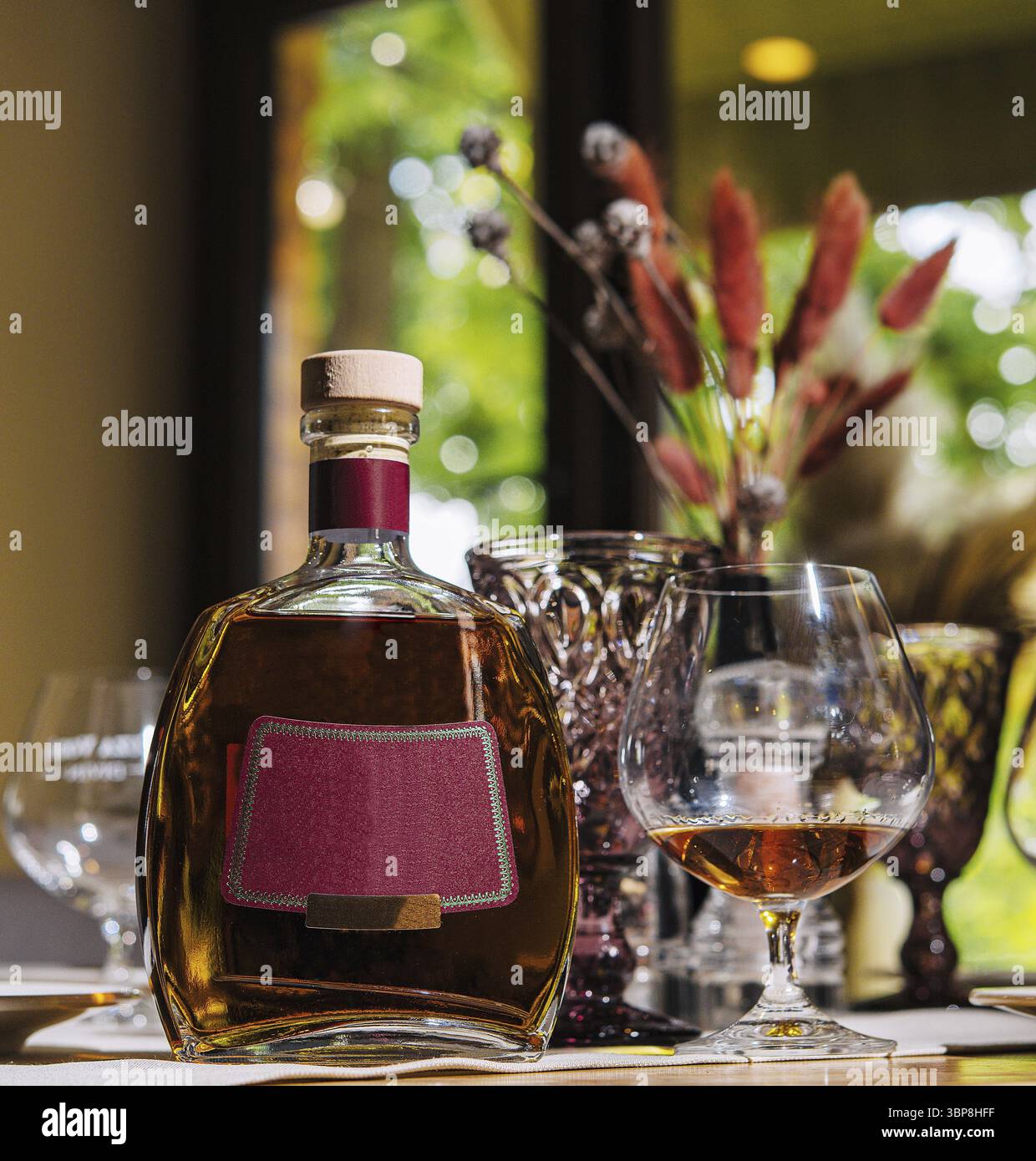 Nourriture, bouteille d'alcool avec une étiquette bleue et un verre sont assis sur une table dans un restaurant, avec une fenêtre en arrière-plan Banque D'Images