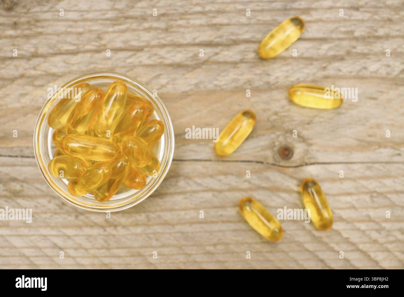 Bol en verre avec capsules d'huile de poisson sur fond en bois, vue de dessus Banque D'Images