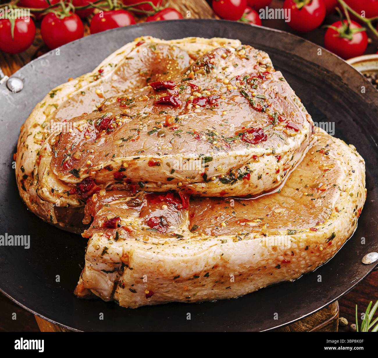 Nourriture, côtelettes de porc fraîches sont recouvertes d'une marinade savoureuse d'herbes et d'épices, prêtes à être grillées pour un barbecue d'été. Tomates cerises dans le dos Banque D'Images
