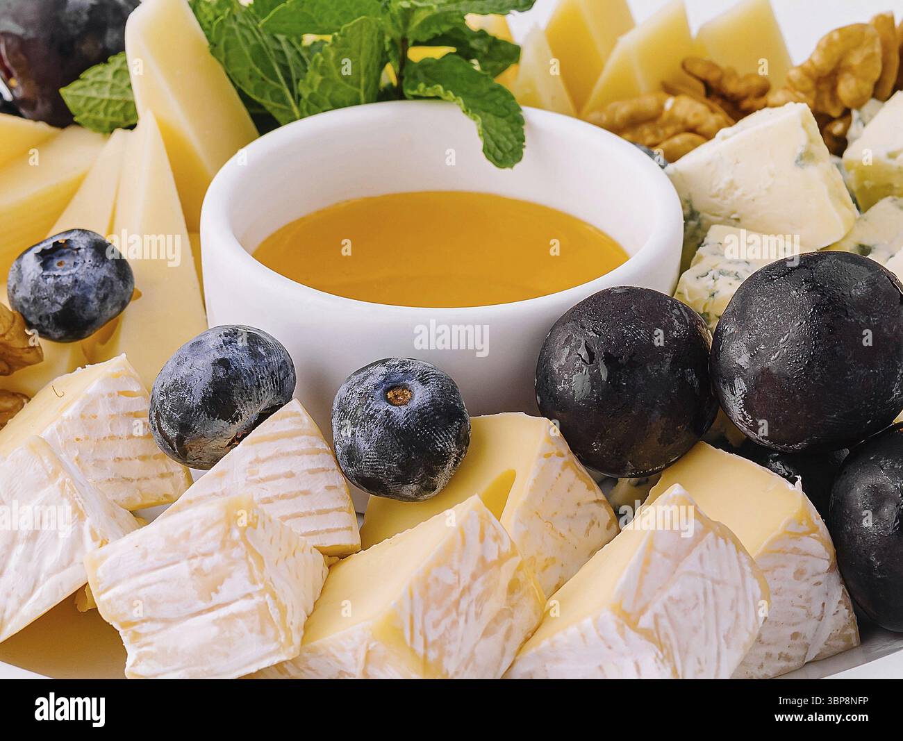 Nourriture, assiette de fromage élégante avec une variété de fromages, noix, bleuets, et un bol de miel de près Banque D'Images