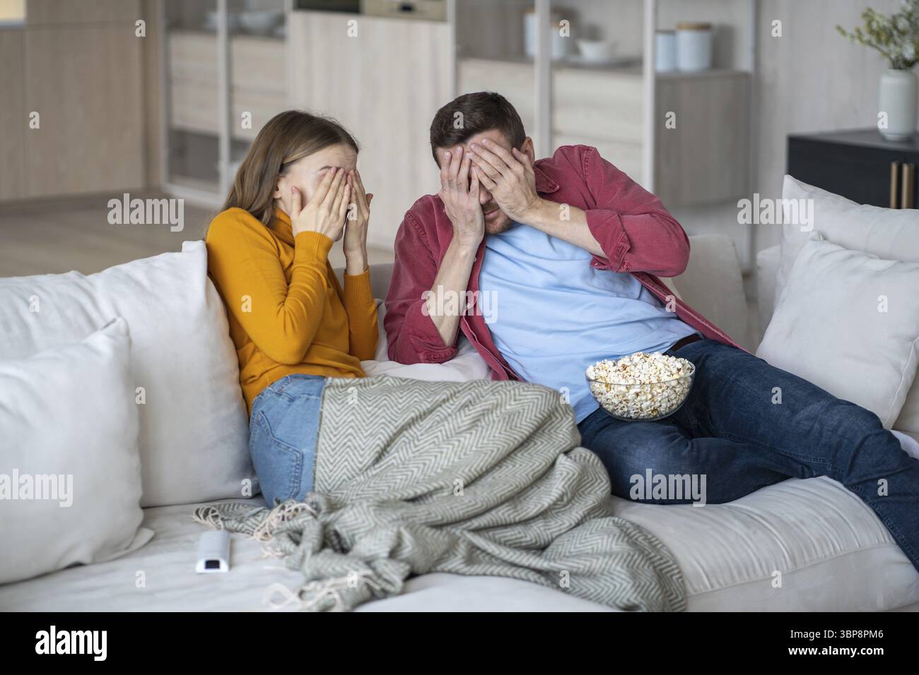 Homme choqué et femme fermant les visages avec les mains effrayées par le thriller terrifiant. Couple de famille effrayé regardant des séries de films ensemble assis sur le canapé Banque D'Images
