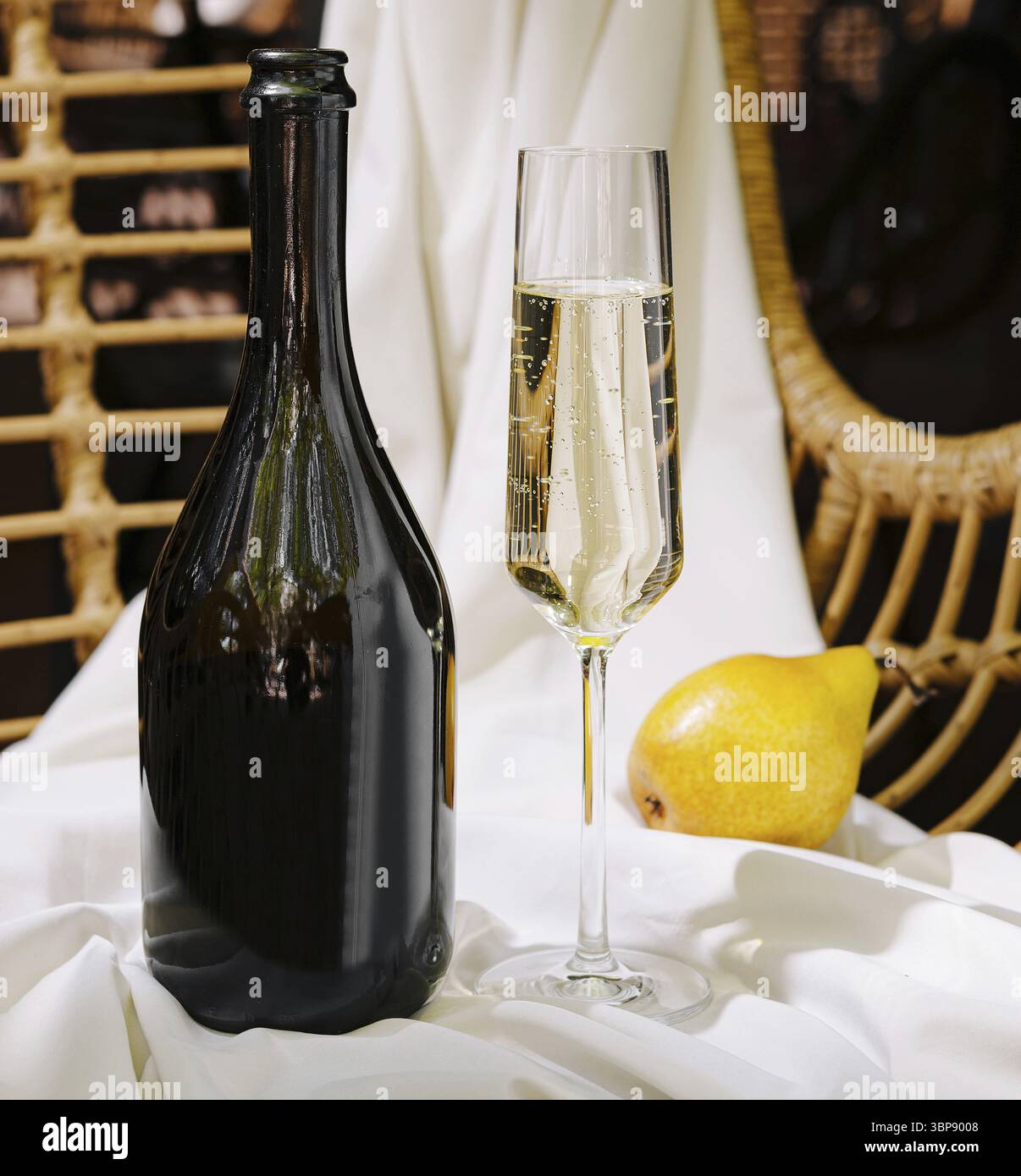 Nourriture, Une bouteille sombre se tient à côté d'un verre rempli de boisson pétillante, avec une poire jaune fraîche reposant sur un tissu blanc doux. Le cadre respire l'élégance Banque D'Images
