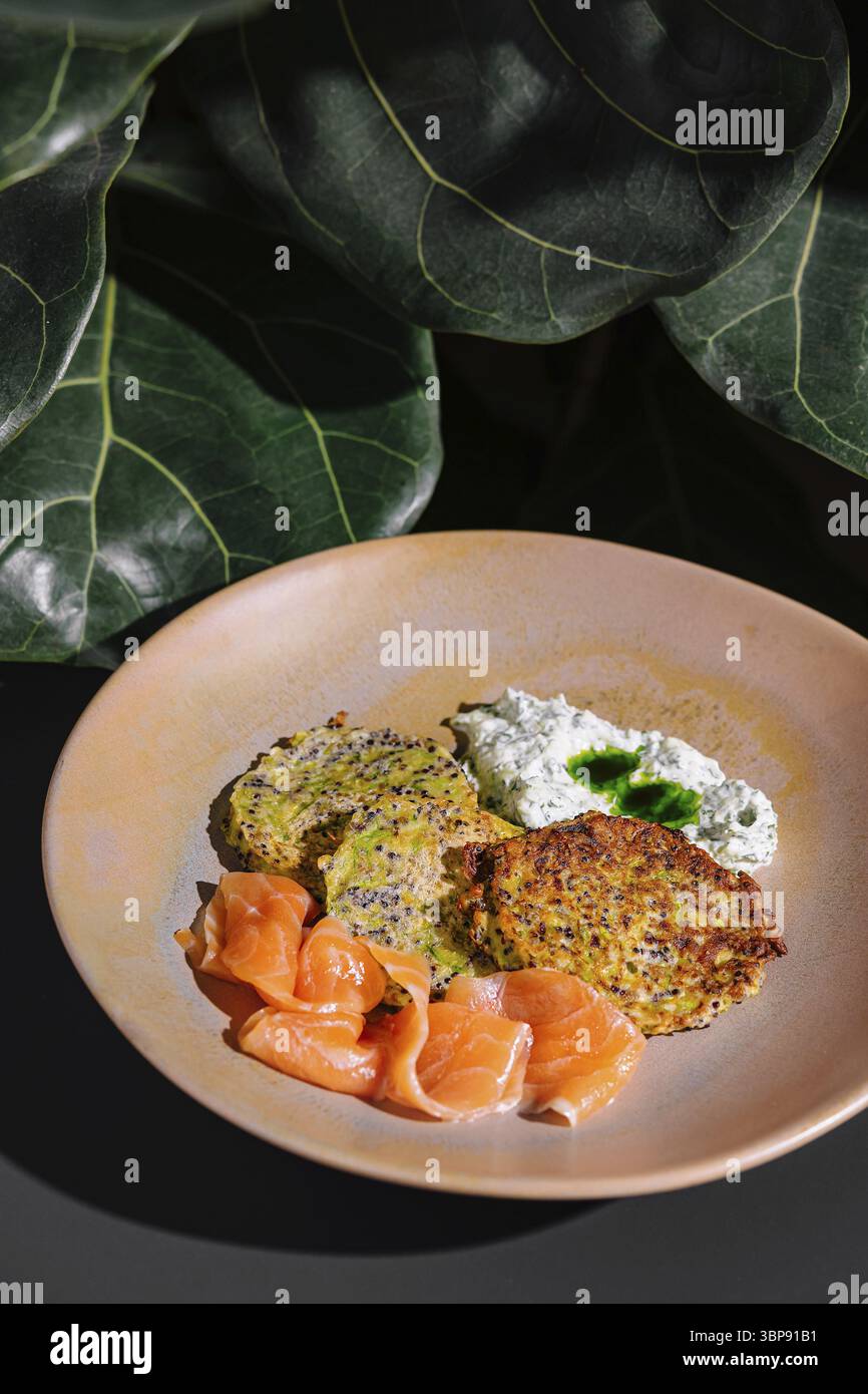Nourriture, beignets de courgettes au saumon et fromage à la crème posés sur une plaque de céramique sous des feuilles vertes Banque D'Images