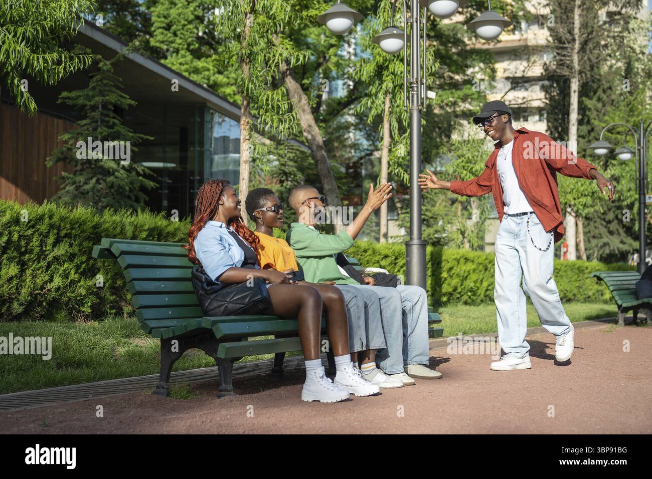 Un étudiant afro-américain ravi court vers des amis noirs assis sur un banc sur le campus universitaire, s'étend la main haute cinq avec un accueil souriant Banque D'Images