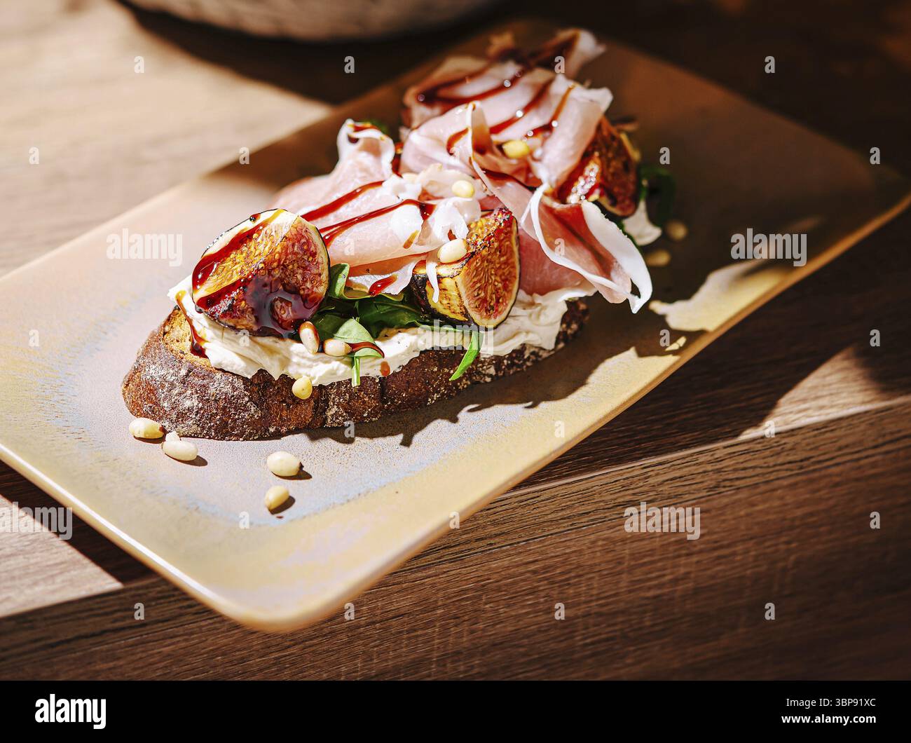 Nourriture, Un sandwich ouvert magnifiquement arrangé avec des figues fraîches, des tranches de jambon et du fromage à la crème sur du pain rustique, garni de pignons de pin. Le w Banque D'Images