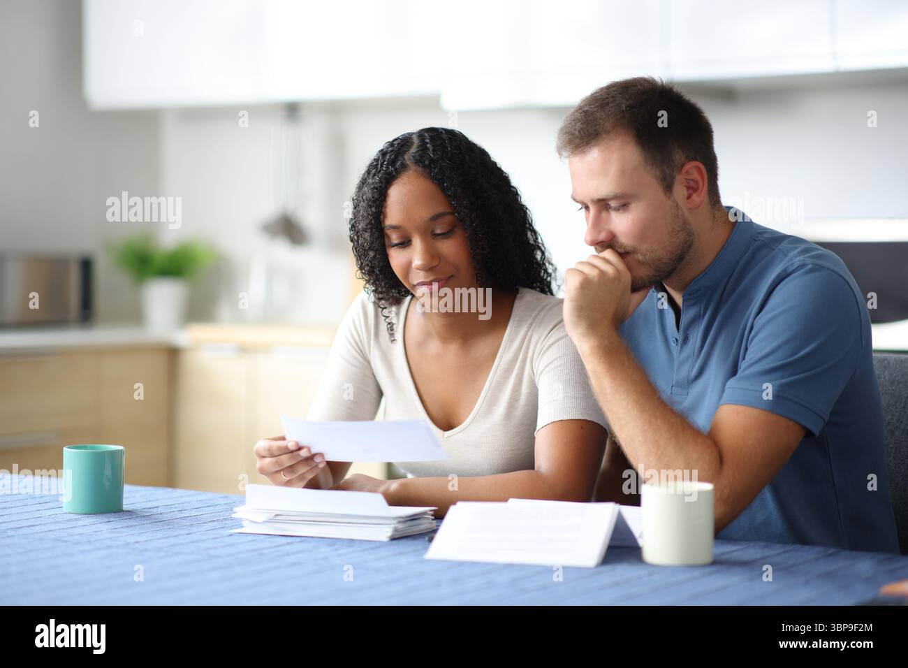 Couple interracial lisant un relevé bancaire dans la cuisine à la maison Banque D'Images