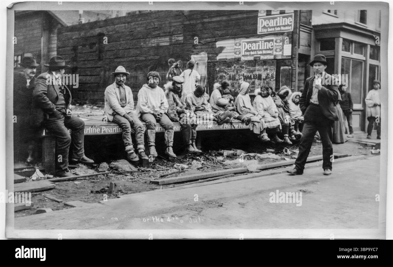 Une lignée d’hommes et de femmes inuits s’assoient tandis que deux hommes blancs occupent l’extrême gauche de l’image à Nome, Alaska, vers 1906-1907. Banque D'Images
