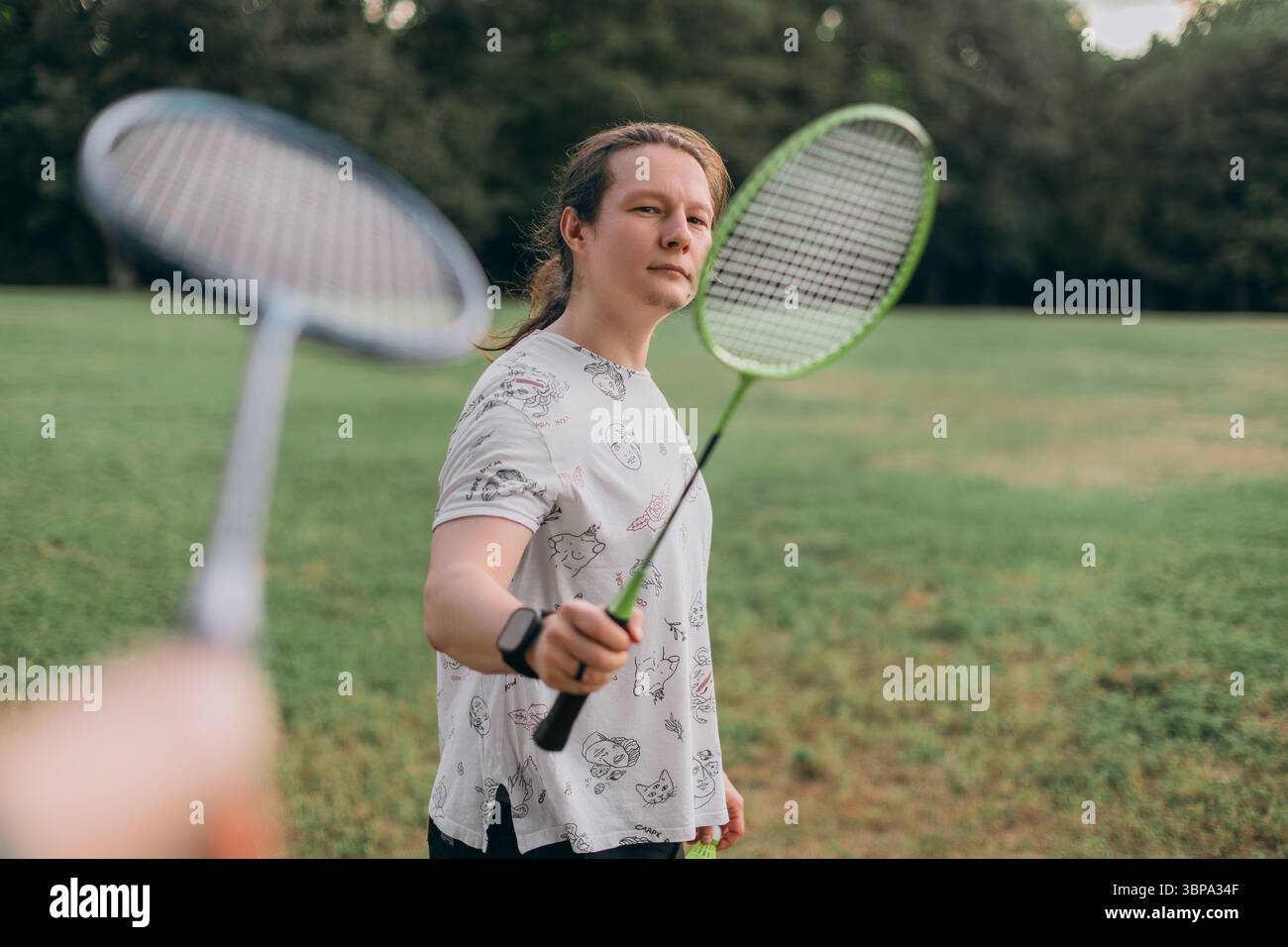 Sérieux homme prêt badminton duel vert champ artistique t-shirt noir shorts smartwatch brillant jour visible raquette adversaire Banque D'Images