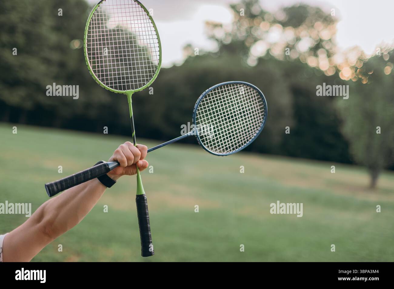 Gros plan de deux raquettes de badminton tenues à l'extérieur sur fond vert flou, ambiance de loisirs d'été Banque D'Images