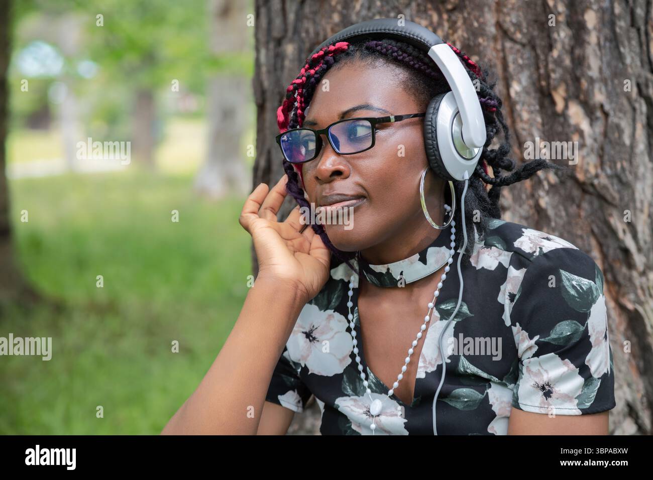 Femme noire avec des lunettes écoutant du contenu audio avec des écouteurs à l'extérieur. Parfait pour les podcasts, la diffusion de musique, l'apprentissage audio, le style de vie numérique Banque D'Images