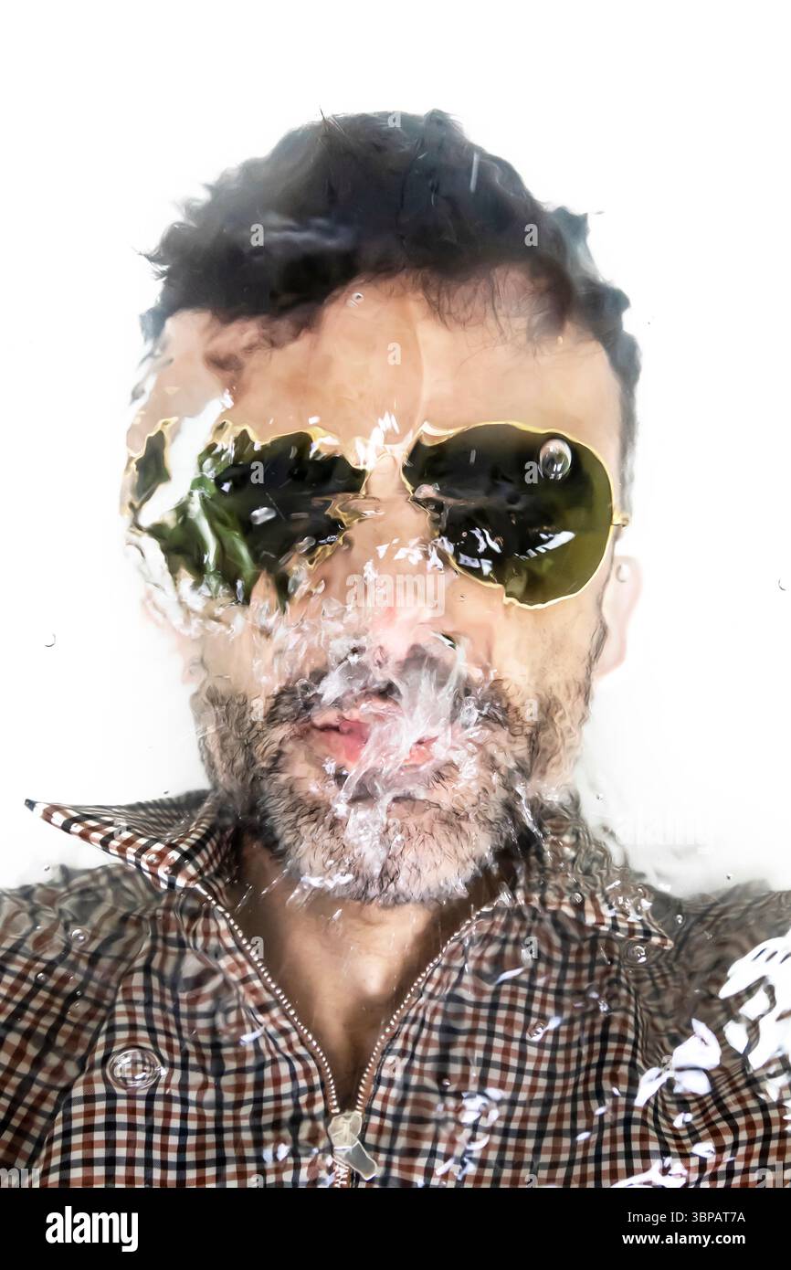 Portrait créatif d'un homme portant des lunettes de soleil, vu à travers une surface de verre texturée ou mouillée, créant un effet visuel déformé et artistique. Banque D'Images