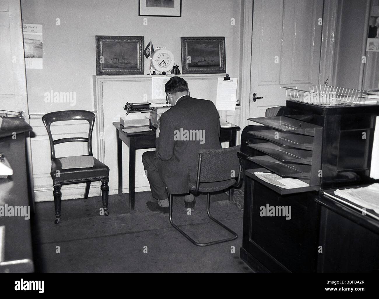 Années 1960, historique, à l'intérieur d'un bureau de ville, un gentleman mature en costume & cravate, assis à un petit bureau en bois, tentant de taper une lettre sur une machine à écrire manuelle, Édimbourg, Écosse, Royaume-Uni. Banque D'Images