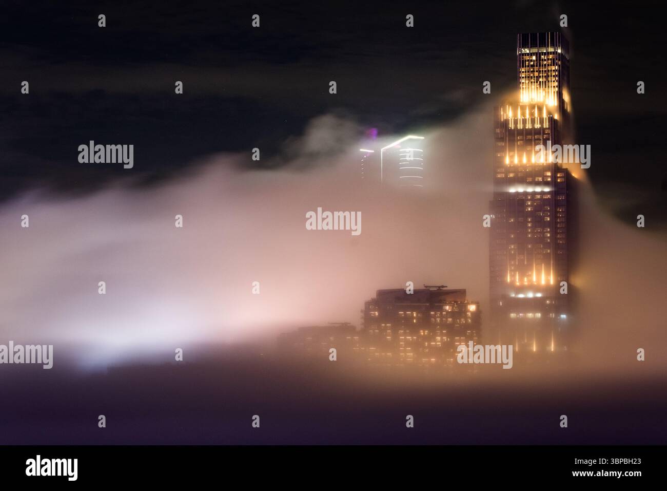 Vue rapprochée des bâtiments commerciaux par une nuit brumeuse à Hong Kong, avec une esthétique cyberpunk avec des lumières brillantes perçant la brume. Banque D'Images