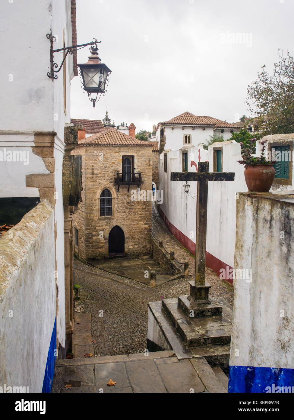 Croix médiévale en pierre et étroite rue pavée dans le centre historique de Óbidos, Portugal Banque D'Images