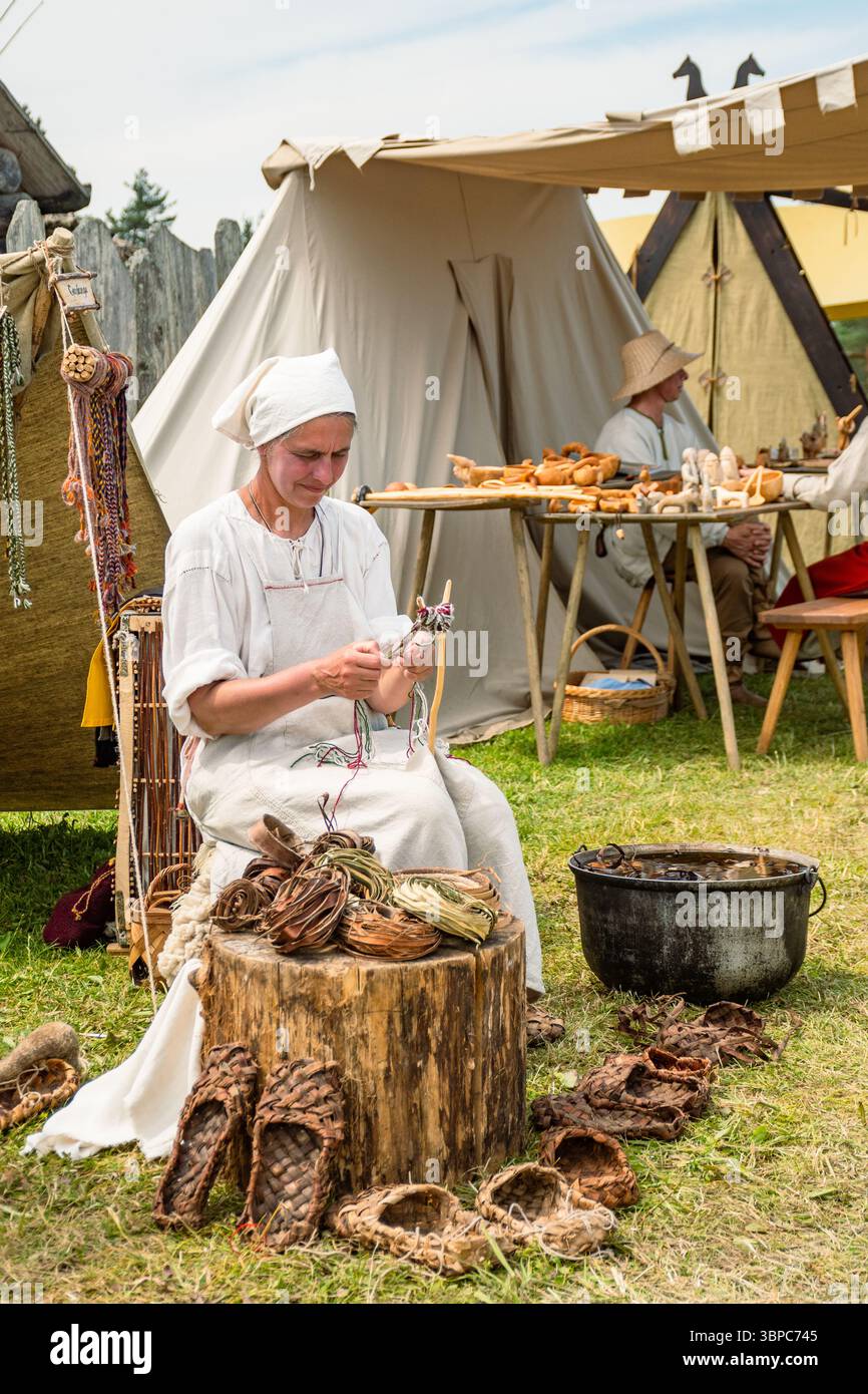 Une femme en habillement médiéval lors d'une fête médiévale fabriquant des chaussures avec le cuir en utilisant une vieille technique utilisée au moyen âge, verticale Banque D'Images