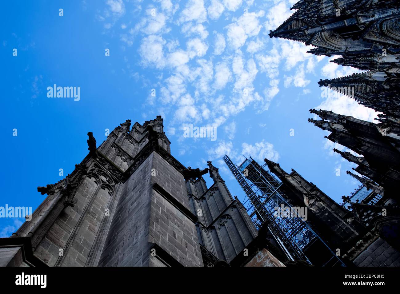 Les tours gothiques de la cathédrale de Cologne s'élèvent puissamment dans un ciel vibrant, capturé d'en bas avec des angles spectaculaires et des détails de pierre, faisant écho à l'histoire Banque D'Images