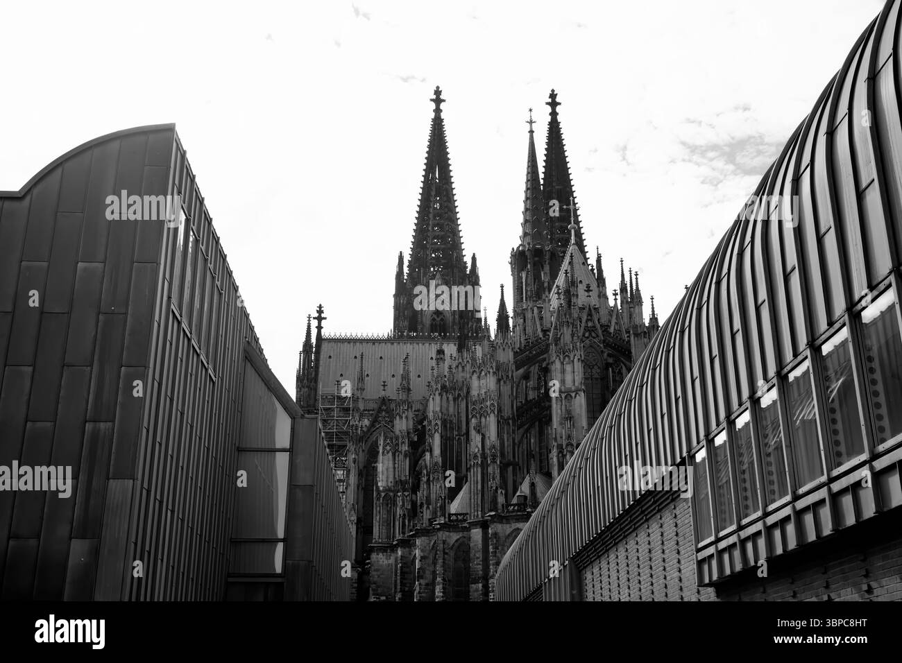 Découvrez les flèches gothiques jumelées de la cathédrale de Cologne qui s'élèvent au-dessus des façades modernes, un dialogue saisissant entre architecture médiévale et forme urbaine contemporaine. Banque D'Images