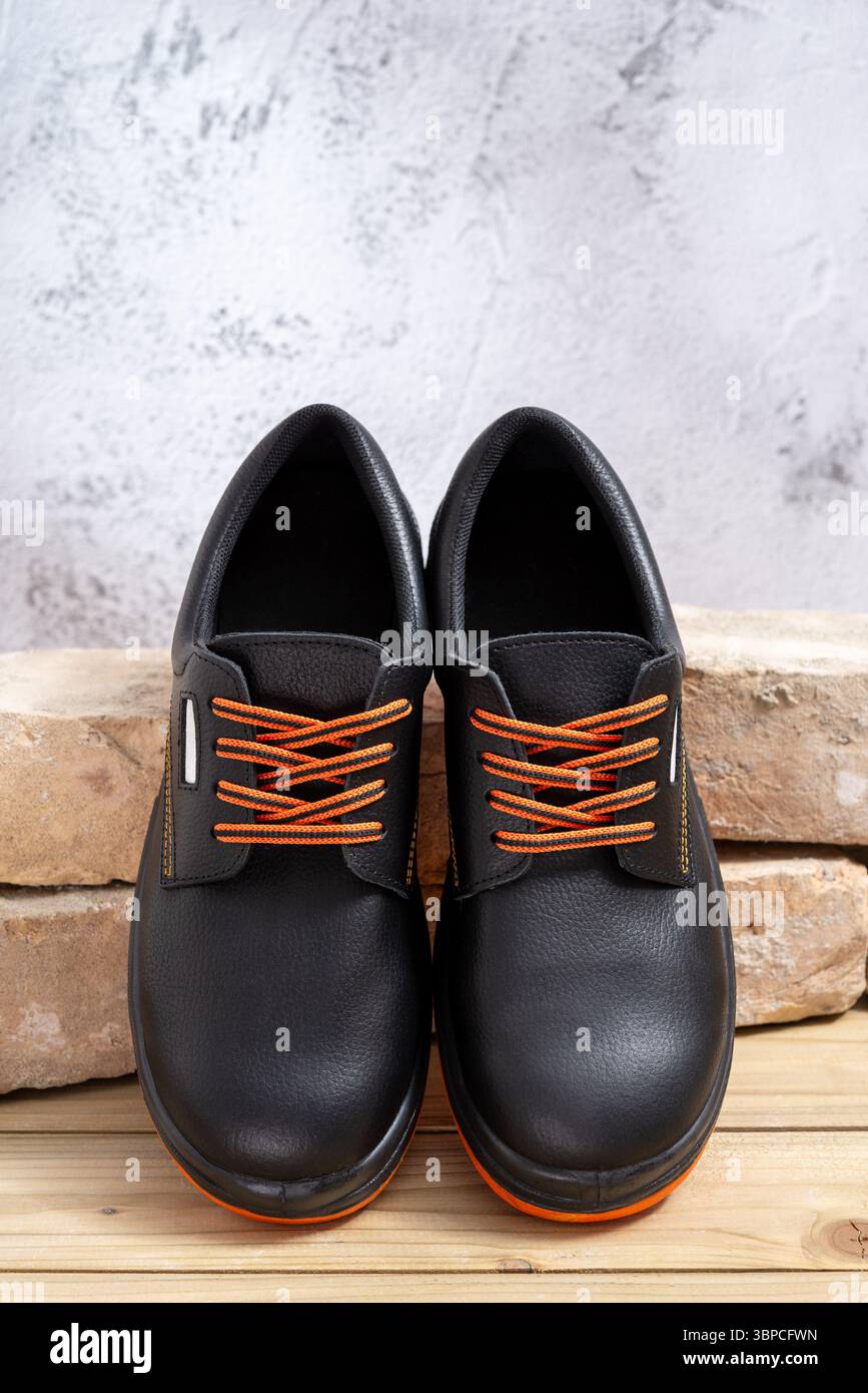 Une paire de nouvelles chaussures de travail appuyées contre de vieilles briques alignées sur une table en bois. Mise au point sélective. Banque D'Images