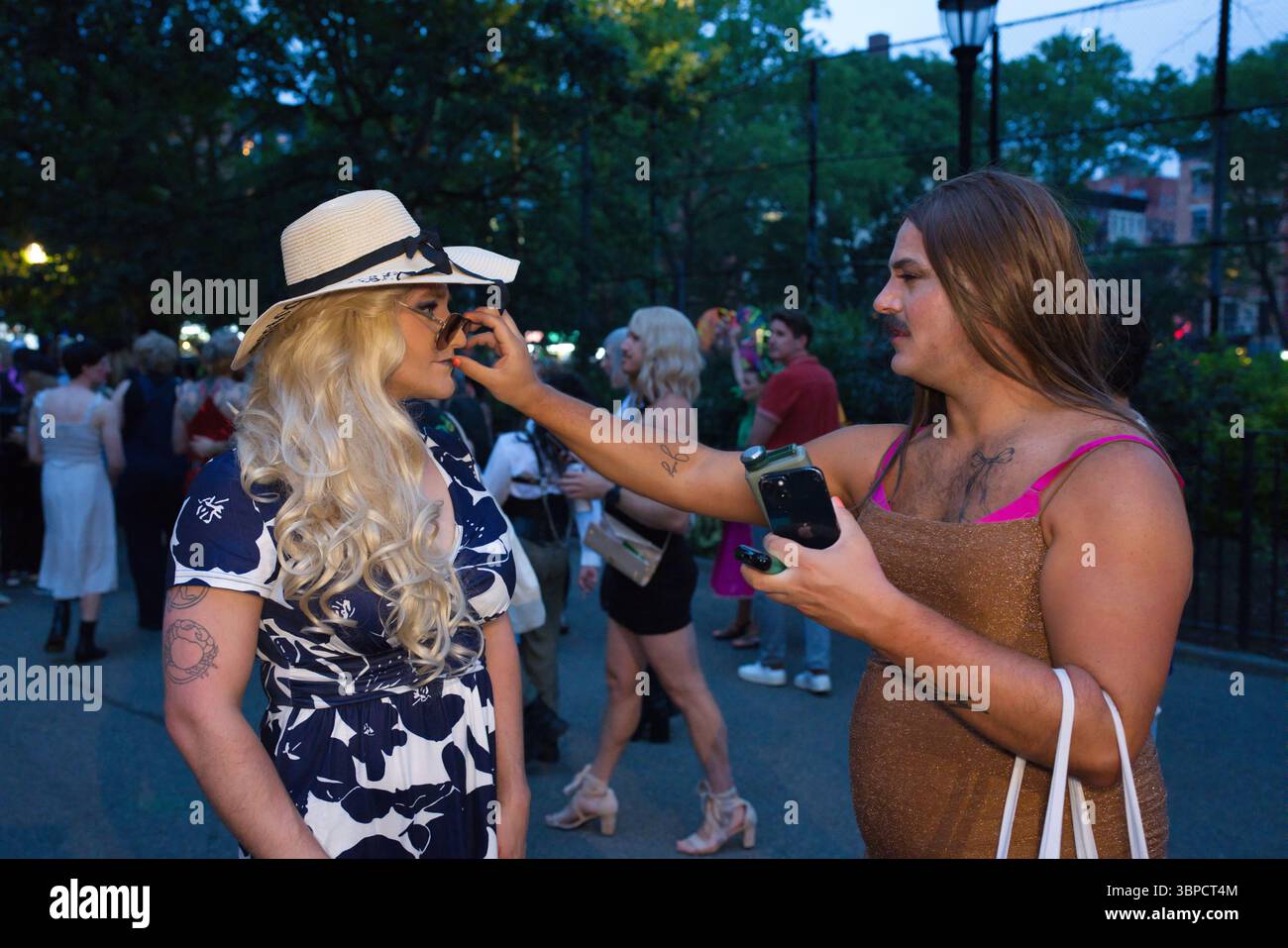 Deux individus, une femme dans une robe florale et un chapeau, l'autre mâle dans une robe dorée, interagissent à l'extérieur au crépuscule. La femme a son sungl Banque D'Images