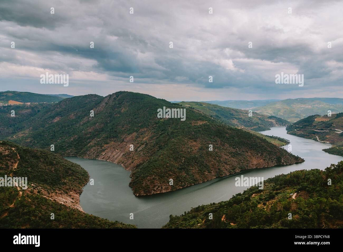 Vue aérienne à couper le souffle de la rivière Tua serpentant à travers des collines verdoyantes et des vallées à Alijo, Vila Real, Portugal, sous un ciel nuageux spectaculaire Banque D'Images
