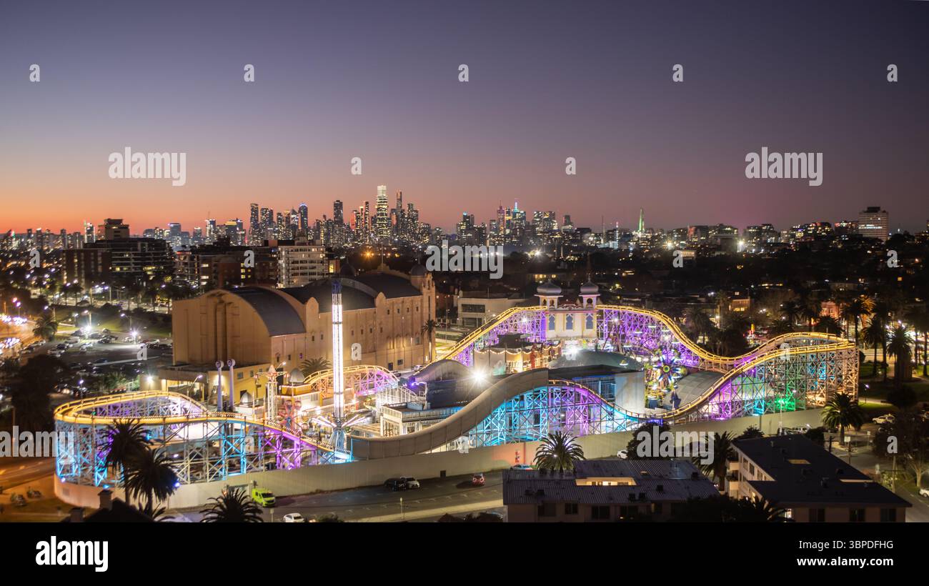 Melbourne Australie. Luna Park à St Kilda s'est illuminé au crépuscule avec Melbourne skyline en arrière-plan. Banque D'Images