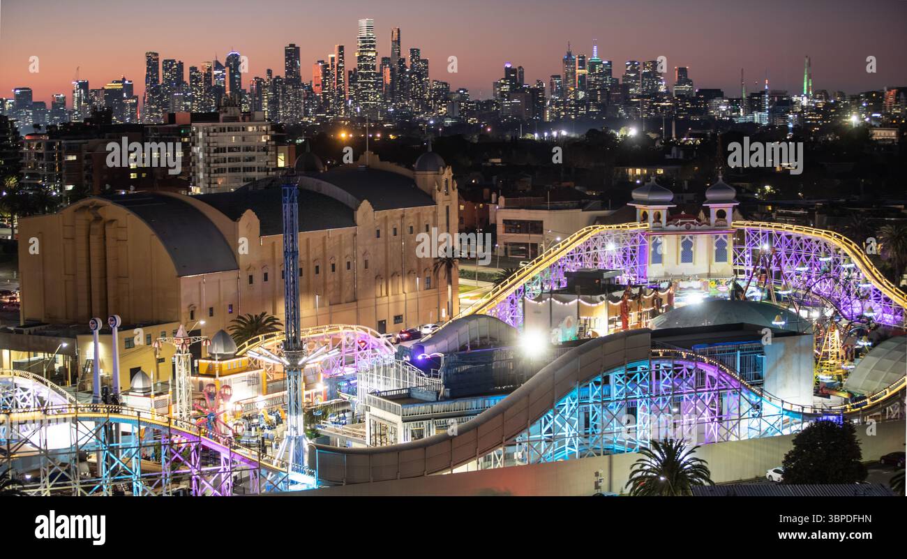 Melbourne Australie. Luna Park à St Kilda s'est illuminé au crépuscule avec Melbourne skyline en arrière-plan. Banque D'Images