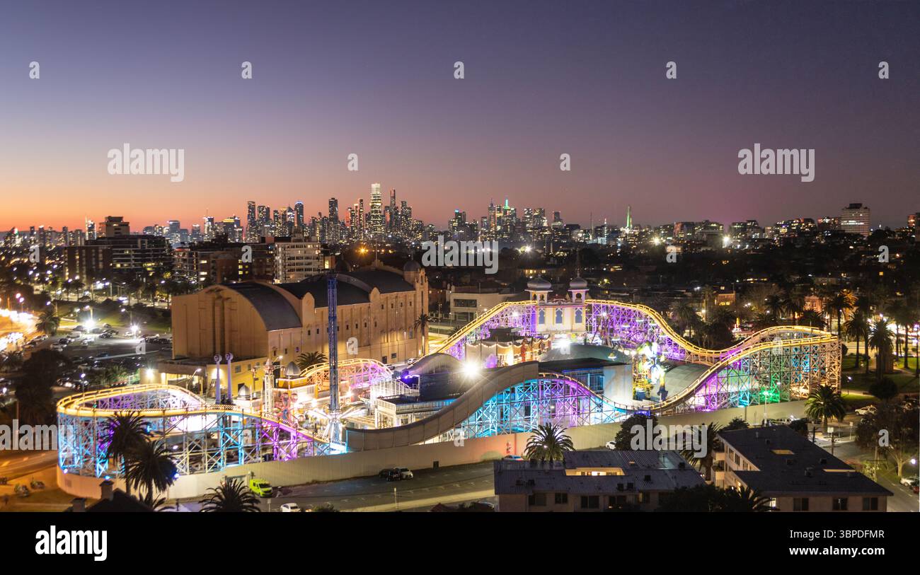 Melbourne Australie. Luna Park à St Kilda s'est illuminé au crépuscule avec Melbourne skyline en arrière-plan. Banque D'Images