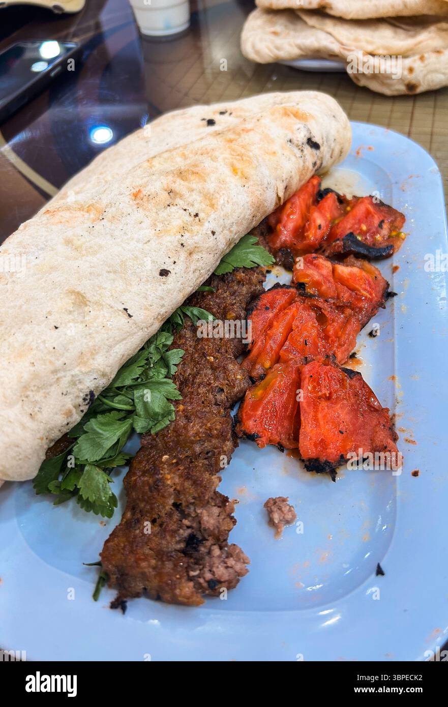 Le pain fraîchement cuit enveloppe le kebab tendre et les tomates carbonisées, créant un repas savoureux apprécié dans la culture culinaire vivante irakienne. Banque D'Images