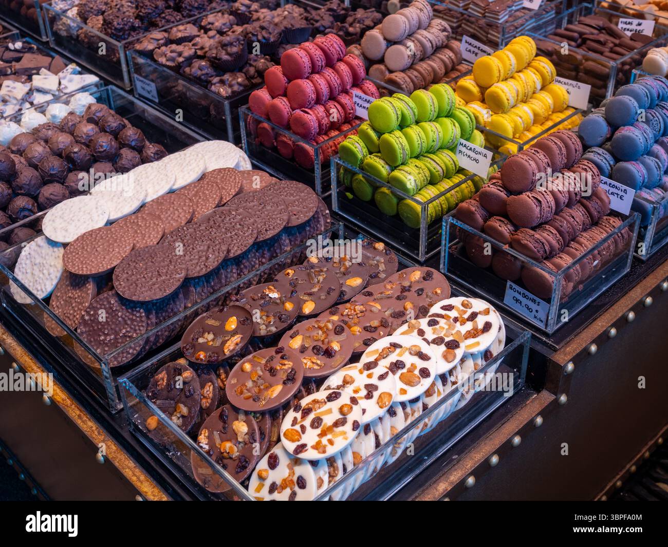 Macarons français colorés et chocolats artisanaux exposés dans un stand de pâtisserie du célèbre marché alimentaire la Boqueria, Barcelone, Espagne. Banque D'Images