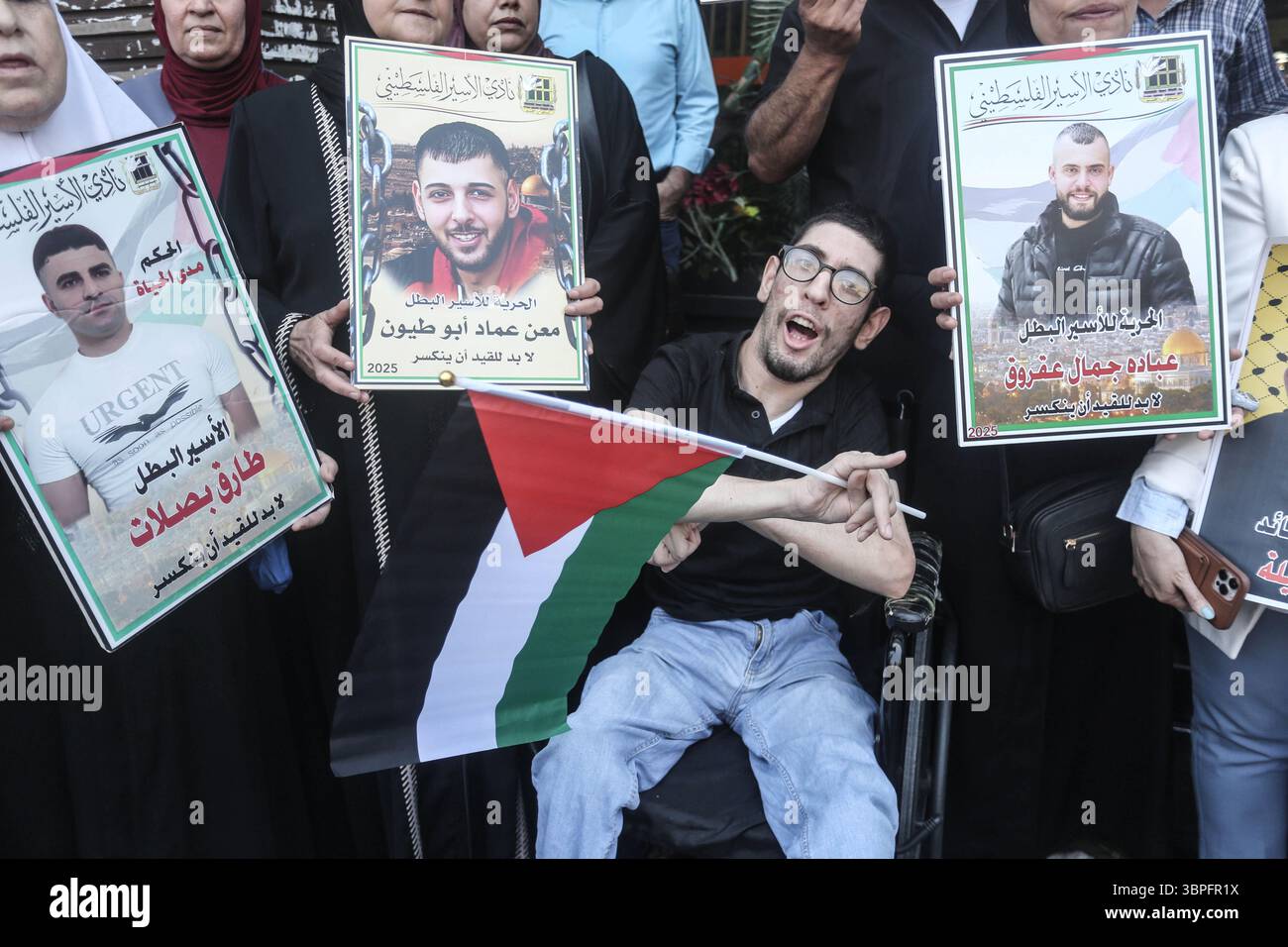Naplouse, Palestine. 08 juillet 2025. Un homme handicapé en fauteuil roulant tient un drapeau et chante un slogan tandis que les familles de prisonniers palestiniens tiennent des photos de leurs proches emprisonnés lors d'un rassemblement de solidarité. Les Palestiniens ont organisé une manifestation pour exiger un accord d'échange de prisonniers avec le gouvernement israélien et le Hamas. Crédit : SOPA images Limited/Alamy Live News Banque D'Images